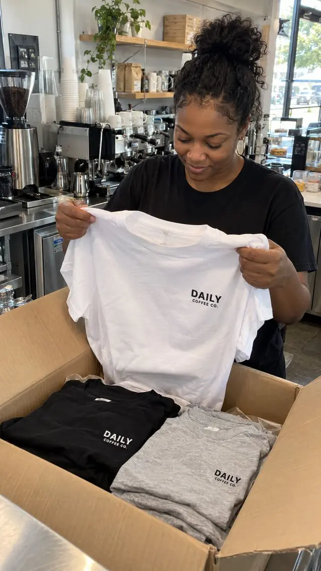 Coffee shop owner unboxing staff tees with a small chest logo